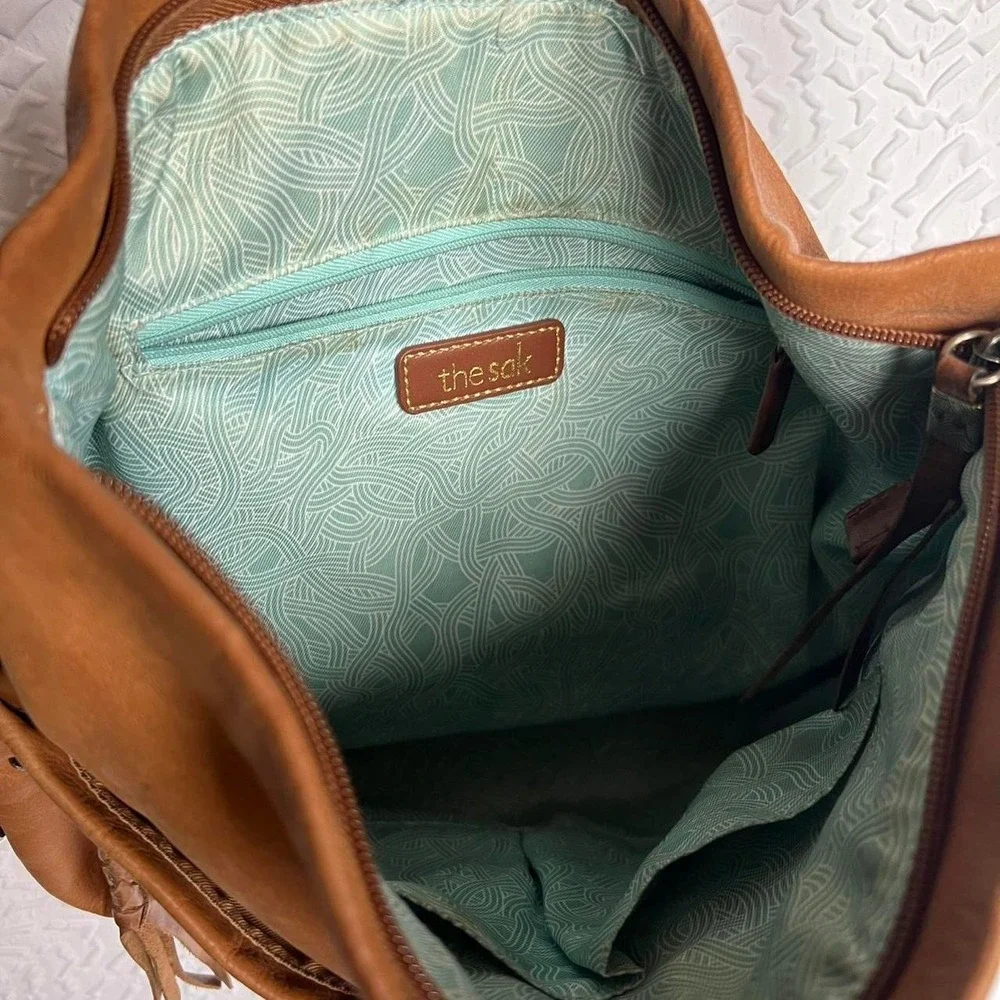 Tan leather shoulder bag with zipper closure, multiple pockets & braided tassel